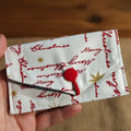 Fabric pouch with Christmas text and a red button on a dark background