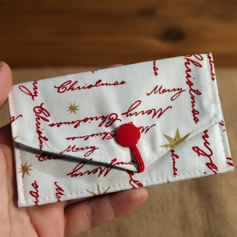 Fabric pouch with Christmas text and a red button on a dark background